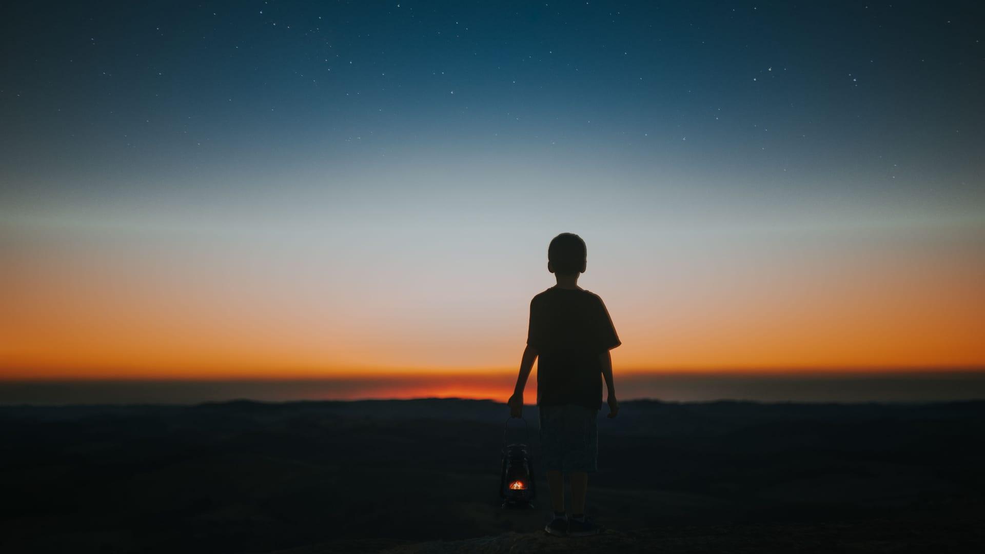 A child's silhouette holding a lantern beneath a dusky sky